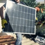 Technician carrying solar panel on rooftop. Clean energy installation outdoors.